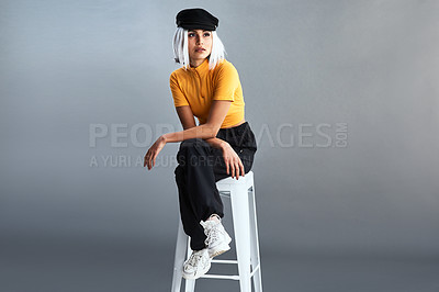 Buy stock photo Studio shot of a beautiful young woman sitting on a stool against a grey background
