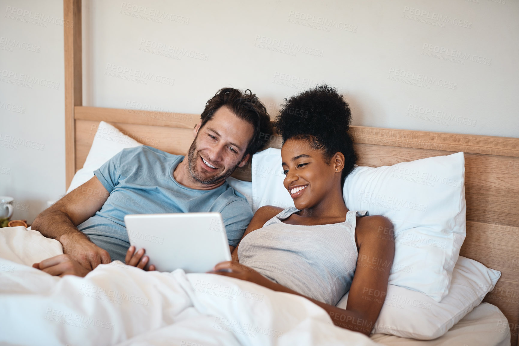Buy stock photo Happy couple, tablet and relax on bed for entertainment, movie or online streaming together at home. Interracial man and woman relaxing, morning or watching on technology or social media in bedroom