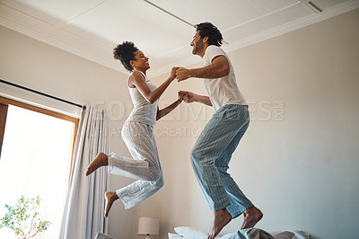 Buy stock photo Shot of a young couple jumping on their bed while holding hands