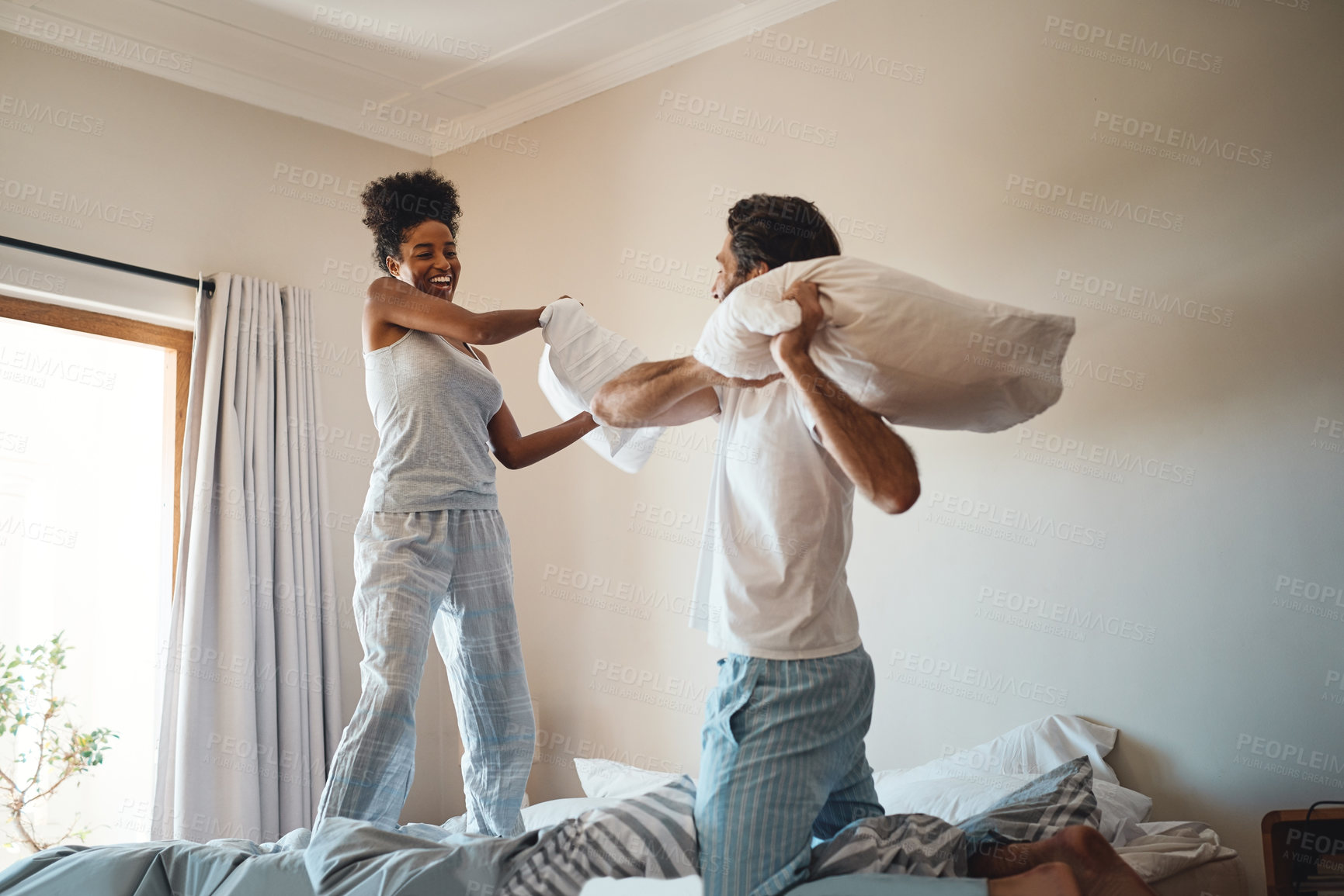 Buy stock photo Pillow fight, playing and bonding with a happy couple playing, bonding and spending time together in their bedroom at home. Laughing, having fun and feeling carefree in pyjamas over the weekend
