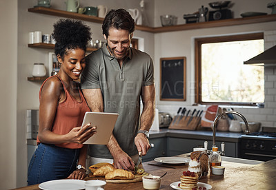 Buy stock photo Young couple cooking healthy food together following recipes online on a tablet, step by step. Happy, cheerful and smiling husband and wife making dinner in the kitchen at home. 