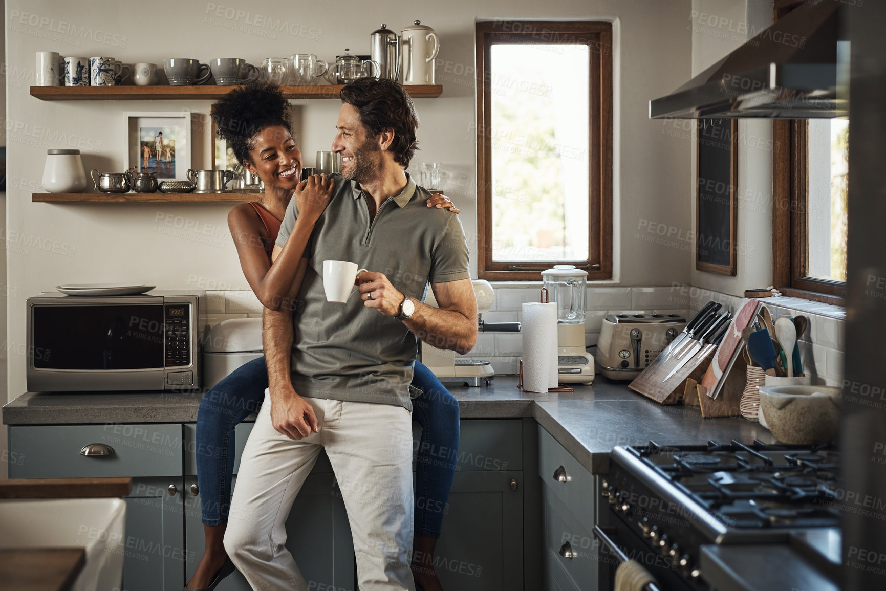 Buy stock photo Happy, in love and laughing while an interracial couple enjoys morning coffee and bonding while having good communication in a relationship. Husband and wife talking while standing in kitchen at home