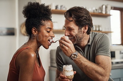 Buy stock photo Romantic, happy and interracial couple eating a healthy yogurt together in a cute, sweet and fun kitchen romance. Loving, in love and excited husband feeding his beautiful afro wife delicious dessert