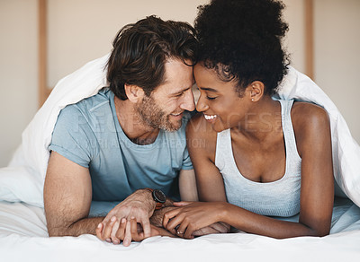 Buy stock photo Happy interracial couple, bed and intimate morning in relax or bonding relationship at home. Man and woman smiling in joyful happiness for love, affection or relaxing weekend together in the bedroom
