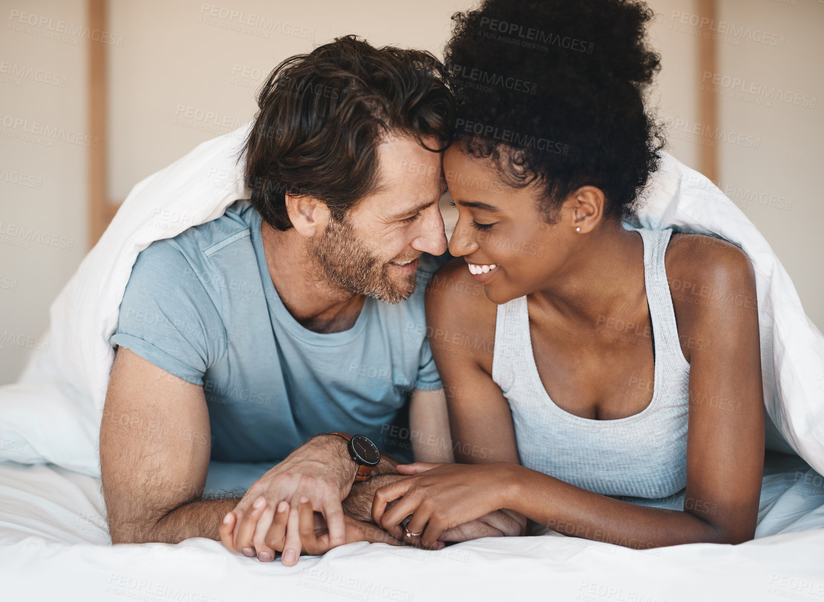 Buy stock photo Happy interracial couple, bed and intimate morning in relax or bonding relationship at home. Man and woman smiling in joyful happiness for love, affection or relaxing weekend together in the bedroom