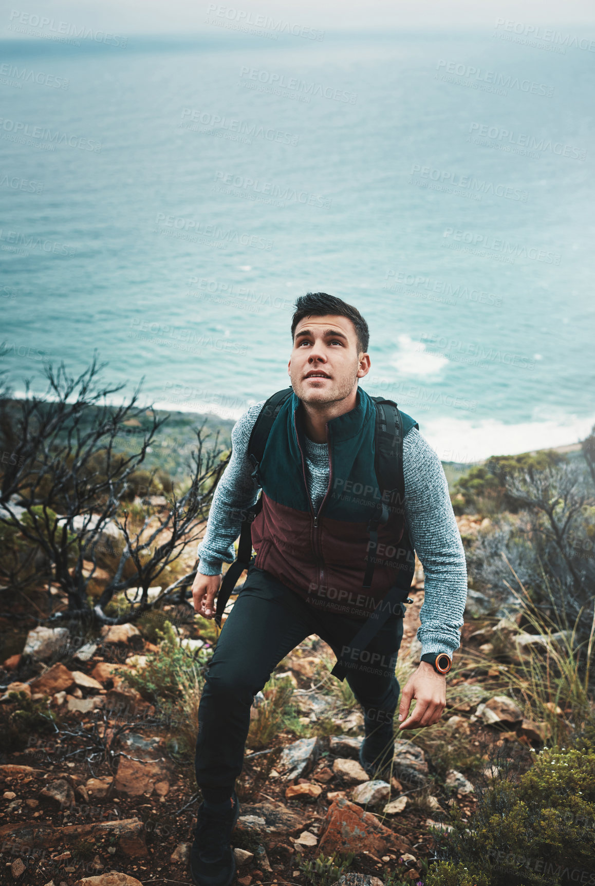 Buy stock photo Shot of a young man hiking through the mountains