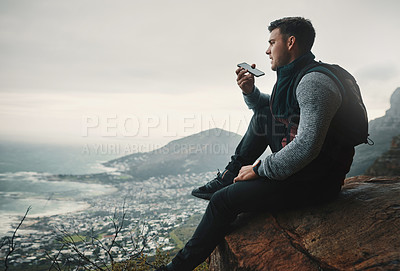 Buy stock photo Shot of a young man talking on a cellphone while sitting on a mountain cliff