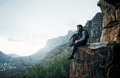 Buy stock photo Shot of a young man looking at the view while sitting on a mountain cliff