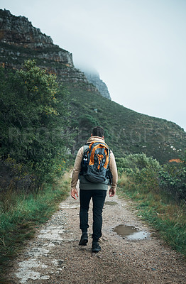 Buy stock photo Rearview shot of a young man hiking through the mountains