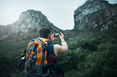 Buy stock photo Shot of a young man taking photos while hiking through the mountains