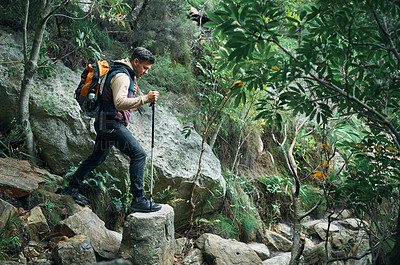 Buy stock photo Shot of a young man using a walking pole while hiking through the mountains