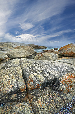Buy stock photo A rocky beach shore and a calm, serene seascape view of the tranquil ocean with blue sky copy space in Camps Bay. An overcast day overlooking ocean boulders in Cape Town, South Africa. 