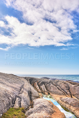Buy stock photo A rocky shore and a seascape view of the ocean with blue sky copy space and a mountain in the background in Camps Bay, Cape Town, South Africa. Calm, serene, tranquil beach and nature scenery