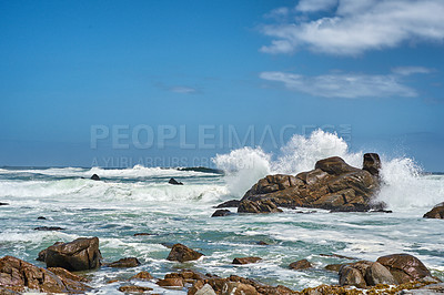 Buy stock photo Big waves splashing and breaking on the coastline. Turbulent sea with rough tides from strong winds crashing onto beach boulders with a blue sky background. Rocky coast in Camps Bay, South Africa