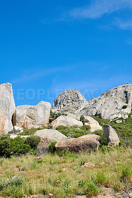 Buy stock photo Copy space with rocks and boulders in rough hiking terrain with blue sky and copyspace. Lush green grass, wild shrubs and flora growing among stone monolith in a quiet nature reserve or countryside
