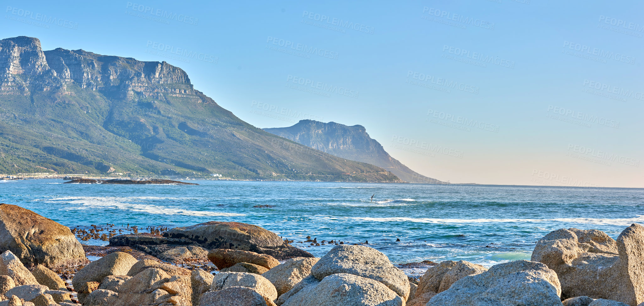 Buy stock photo Quiet and calm ocean with rocky shore and boulders. Scenic seascape of the Twelve Apostles mountain under a blue sky in Cape Town. A beautiful holiday destination for travel and tourism