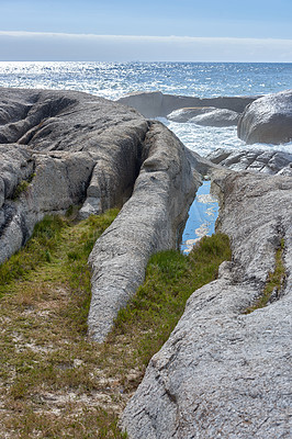 Buy stock photo Copyspace at sea with a blue sky background and rocky coast in Camps Bay South Africa. Ocean waves crashing onto boulders at a beach shore. Peaceful scenic landscape for a relaxing summer holiday
