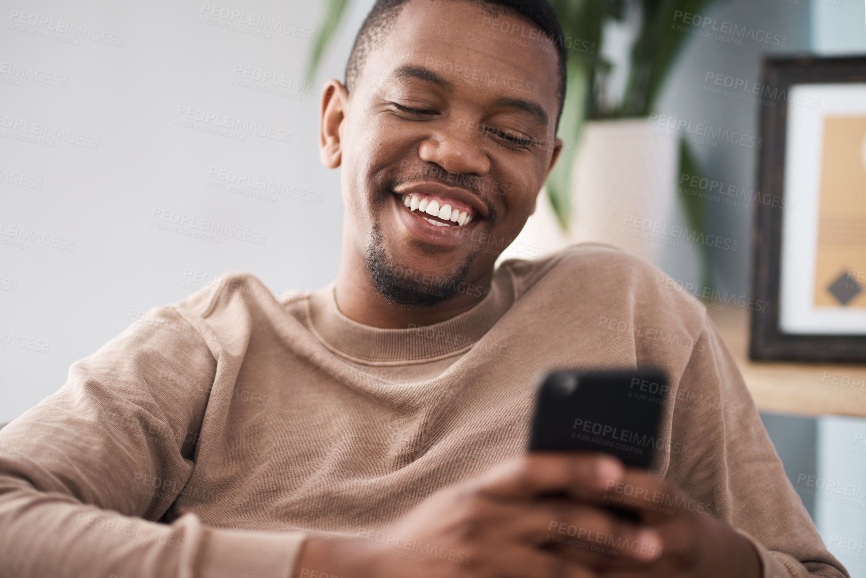 Buy stock photo Black man, phone and smile for social media, communication or texting while relaxing at home. Happy African American male smiling enjoying conversation, chatting or connectivity on mobile smartphone