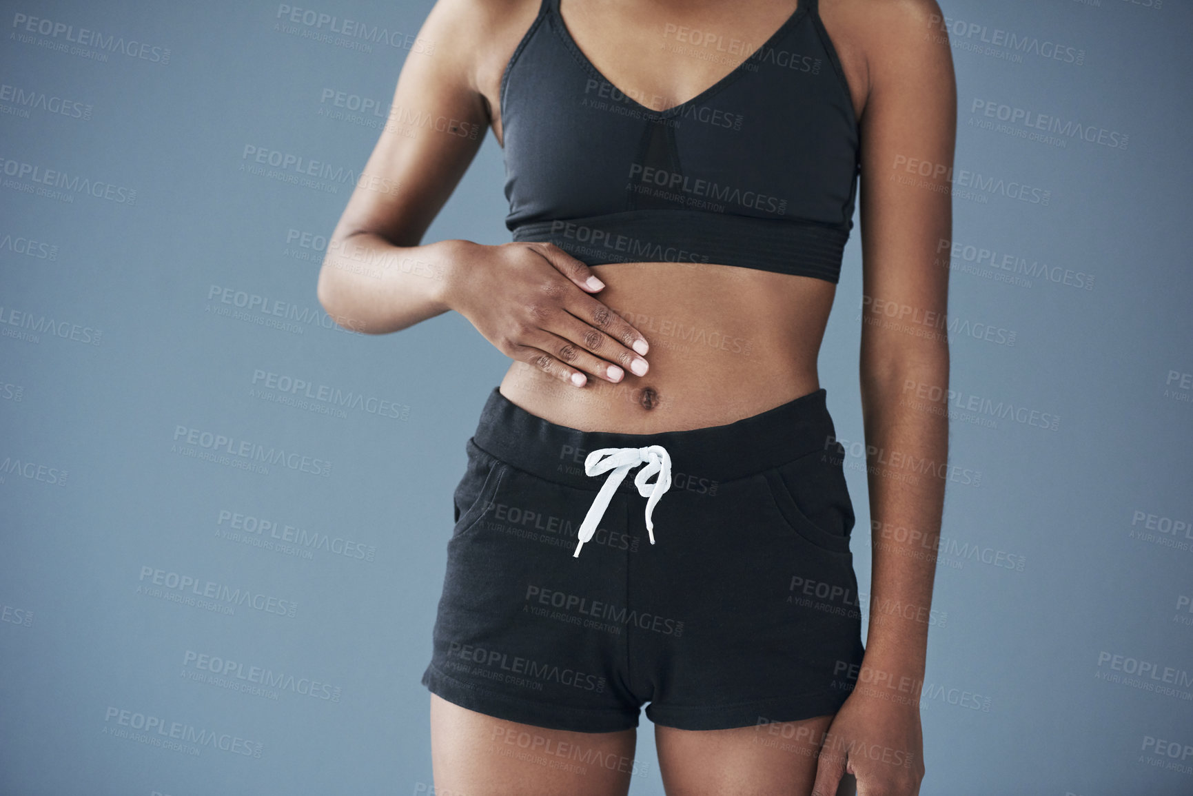 Buy stock photo Body, gut health or hands of woman on stomach and diet to lose weight for fitness or training. Blue background, sportswear or girl athlete touching abdomen in studio for exercise results or digestion