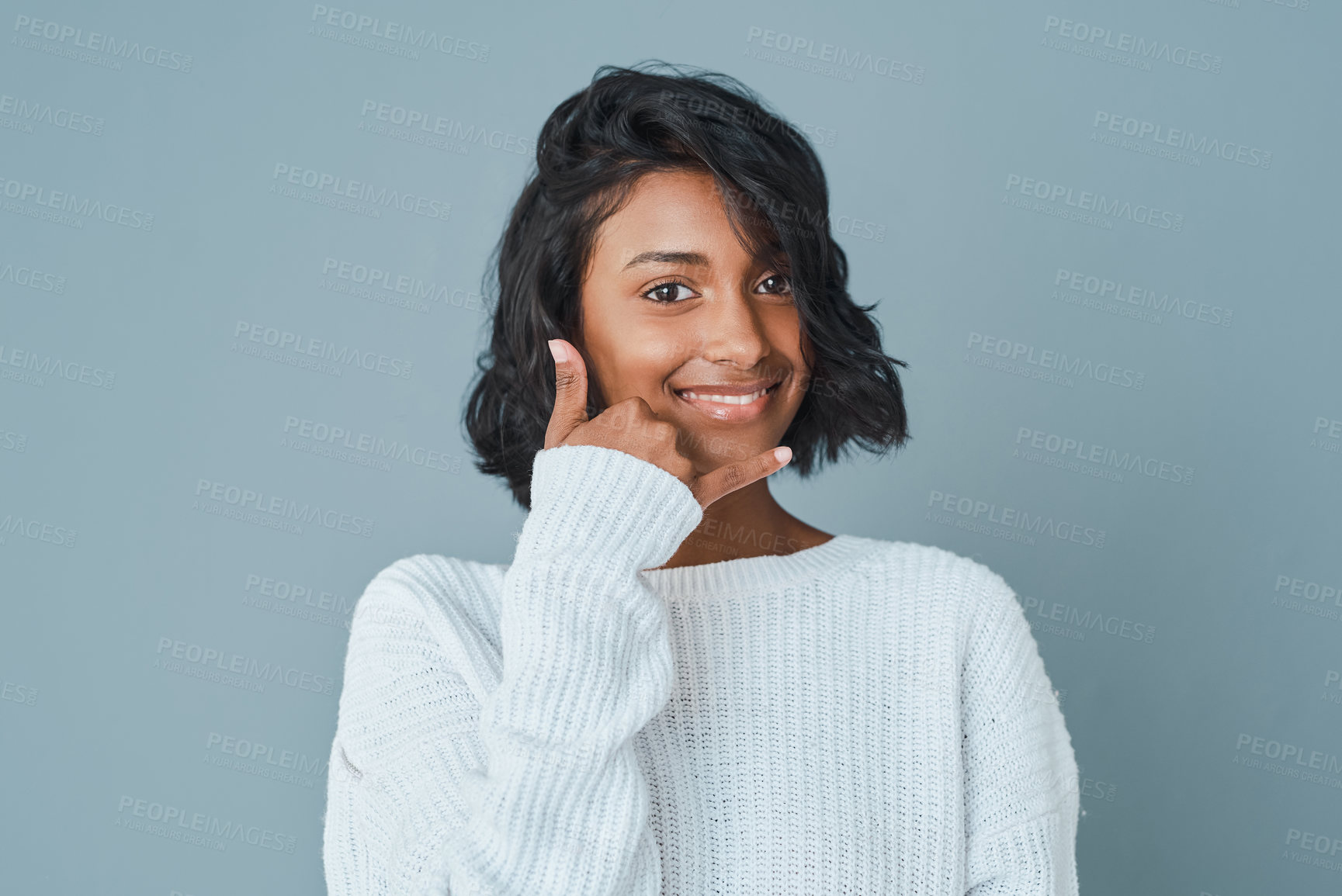 Buy stock photo Portrait, smile and woman in studio with call me hand or emoji isolated on blue background. Confident, signal or happy Indian model with flirting gesture for cellphone chat, hello or communication 