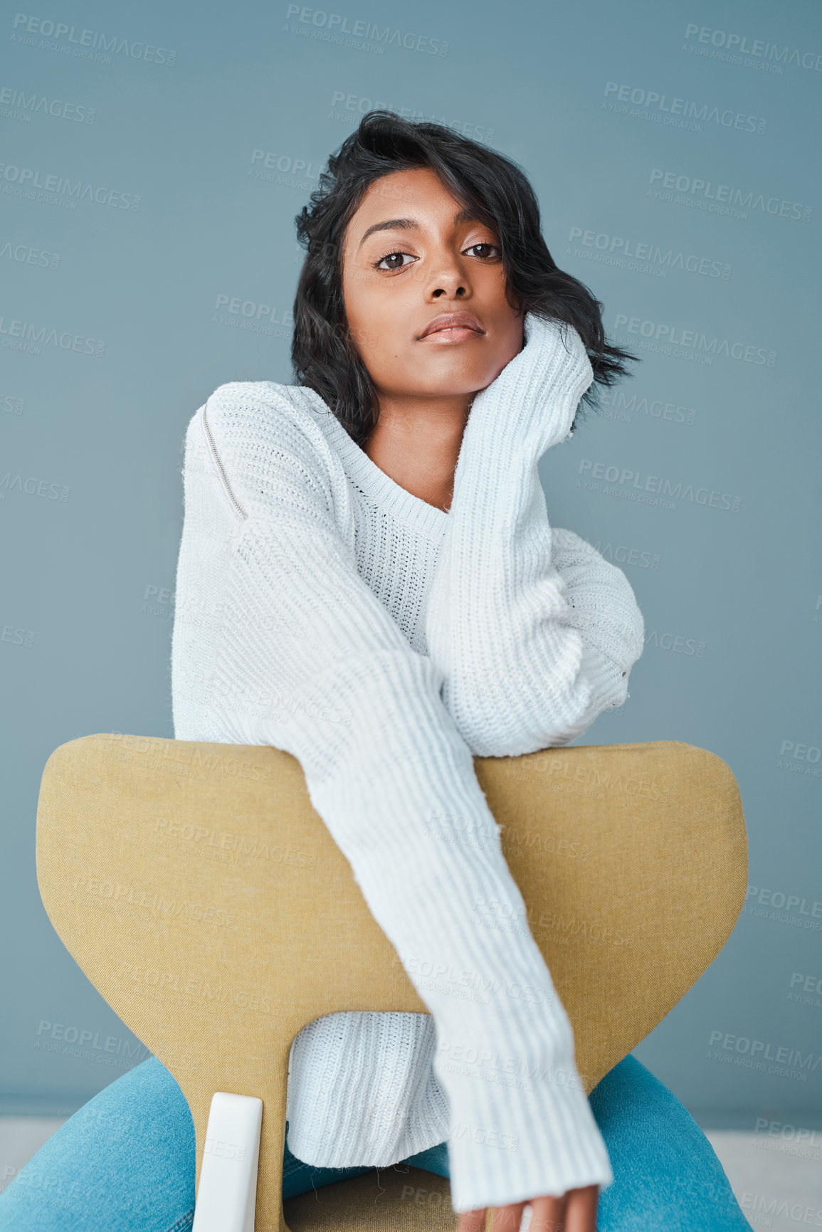 Buy stock photo Relax, student and fashion with portrait of woman in studio for casual, trendy and calm. Sweater, jersey or wool top with Indian person sitting on chair on blue background for confidence in clothes