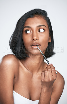 Buy stock photo Indian woman, beauty and makeup with thinking, idea and lip gloss in wellness, routine or facial treatment. Female person, serious and planning for cosmetics, dermatology or glow on studio background