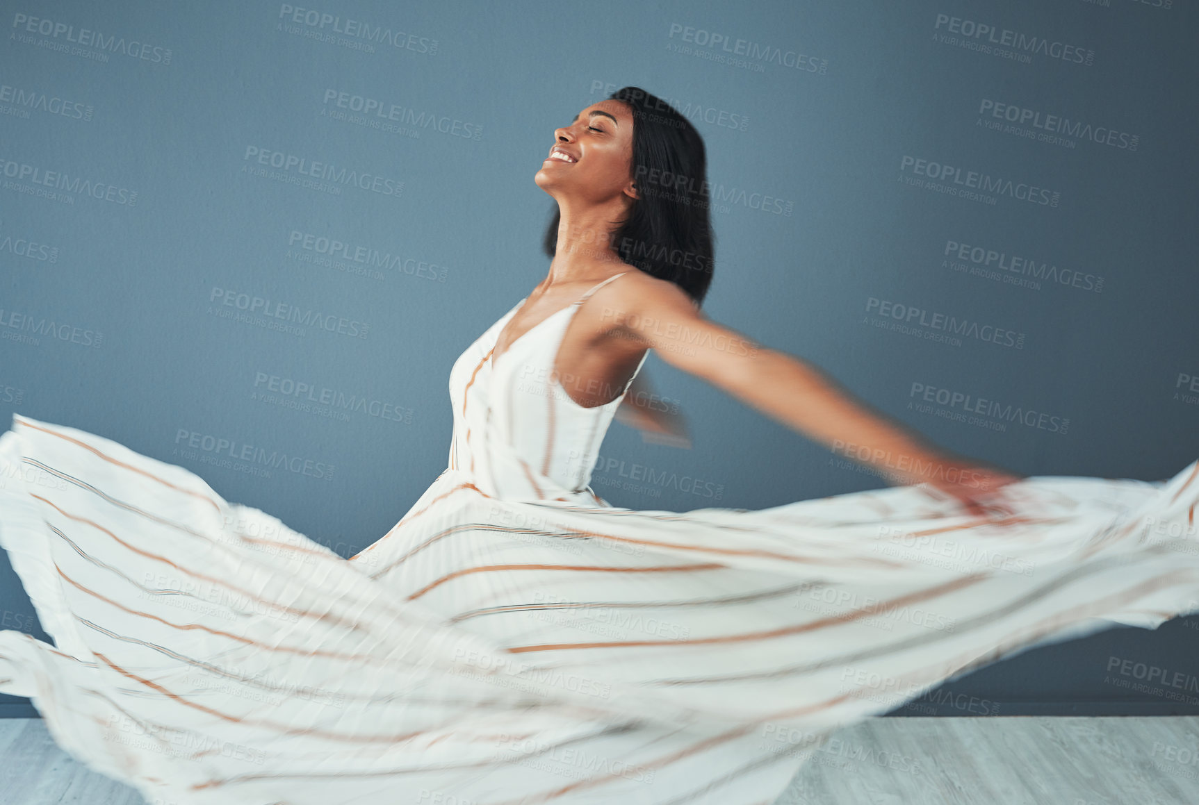 Buy stock photo Shot of a beautiful young woman wearing a long flared dress against a blue background
