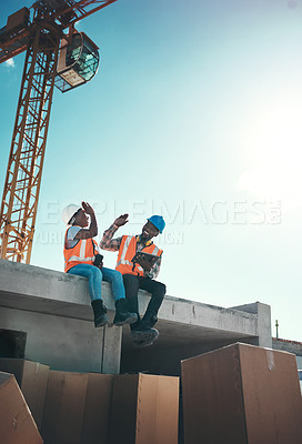Buy stock photo Shot of a young man and woman sitting on top of a building at a construction site and giving each other a high five