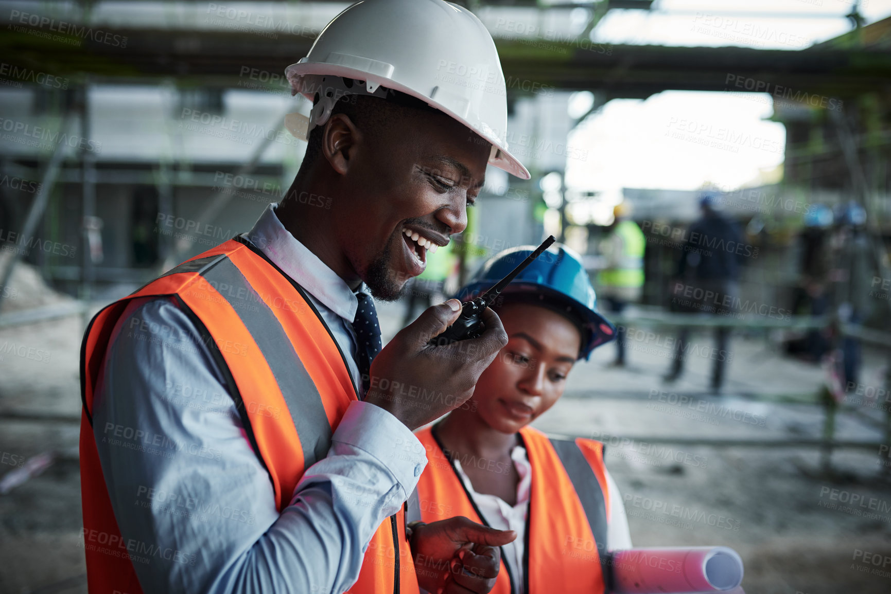 Buy stock photo Shot of a young man using a walkie talkie while working with his colleague at a construction site