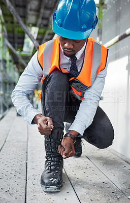 Buy stock photo Shot of a young man tying the shoelaces on his boots while working at a construction site