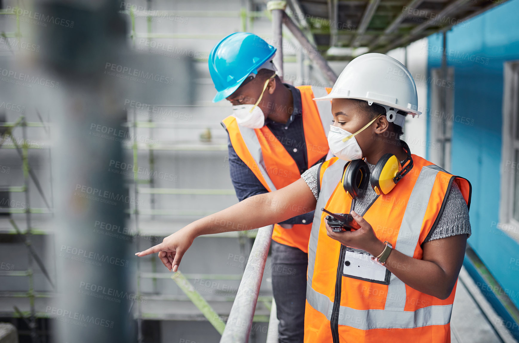 Buy stock photo Shot of a young woman using a walkie talkie while working with her colleague at a construction site