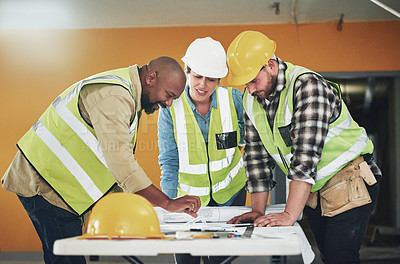 Buy stock photo Shot of a group of builders going over building plans at a construction site