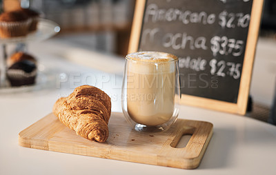 Buy stock photo Closeup shot of a croissant and a cup of coffee on a wooden serving board in a cafe