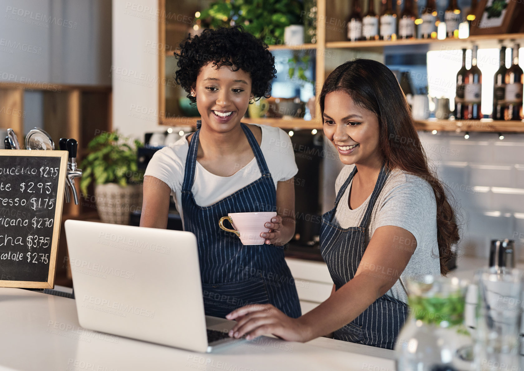 Buy stock photo Women, waitress and happy with laptop at cafe on counter for online orders, ecommerce and purchase. People, employees and smile at coffee shop as barista on internet for social media reviews on menu