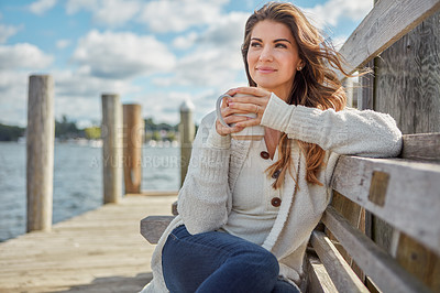 Buy stock photo Shot of a beautiful young woman enjoying a warm beverage while relaxing on a bench at a lake