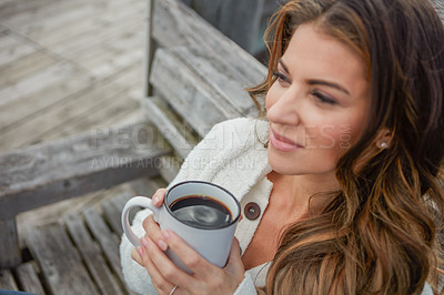 Buy stock photo Shot of a beautiful young woman enjoying a warm beverage while relaxing on a bench outdoors