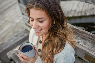 Buy stock photo Shot of a beautiful young woman enjoying a warm beverage while relaxing on a bench outdoors