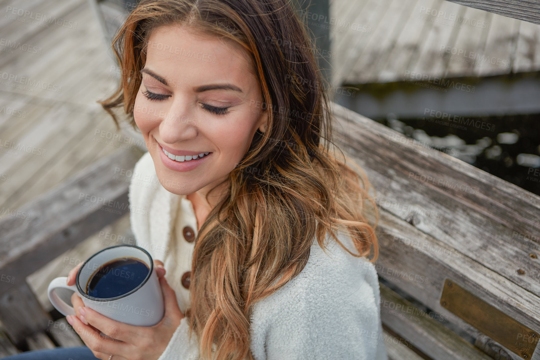 Buy stock photo Shot of a beautiful young woman enjoying a warm beverage while relaxing on a bench outdoors