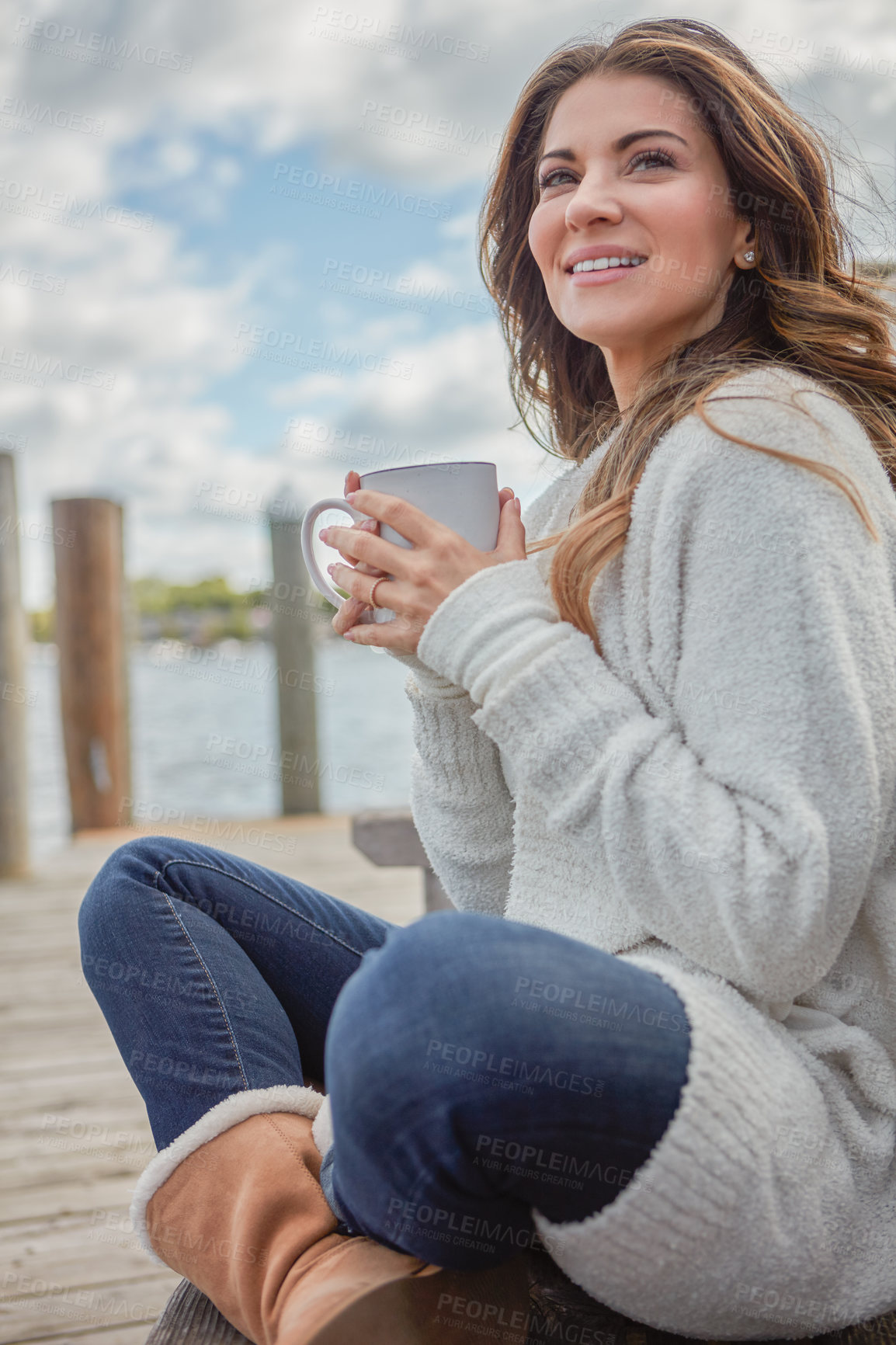 Buy stock photo Shot of a beautiful young woman enjoying a warm beverage while relaxing on a bench at a lake