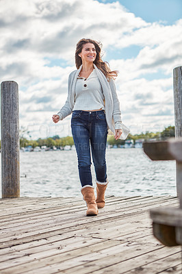 Buy stock photo Shot of a beautiful young woman walking along a pier at a lake
