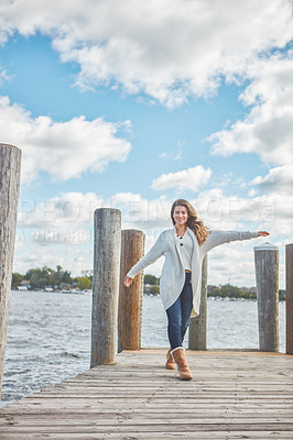 Buy stock photo Shot of a beautiful young woman walking along a pier at a lake