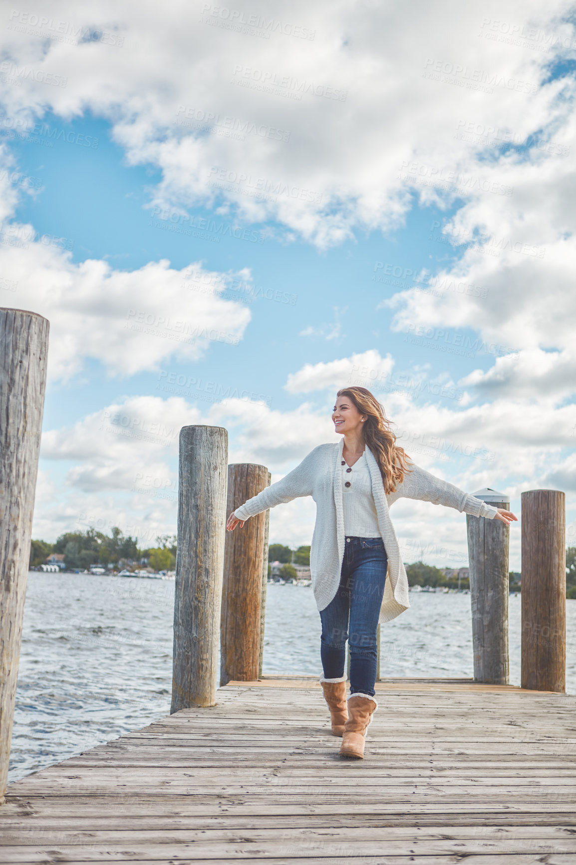 Buy stock photo Shot of a beautiful young woman walking along a pier at a lake