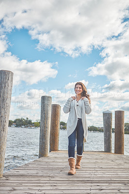 Buy stock photo Shot of a beautiful young woman walking along a pier at a lake