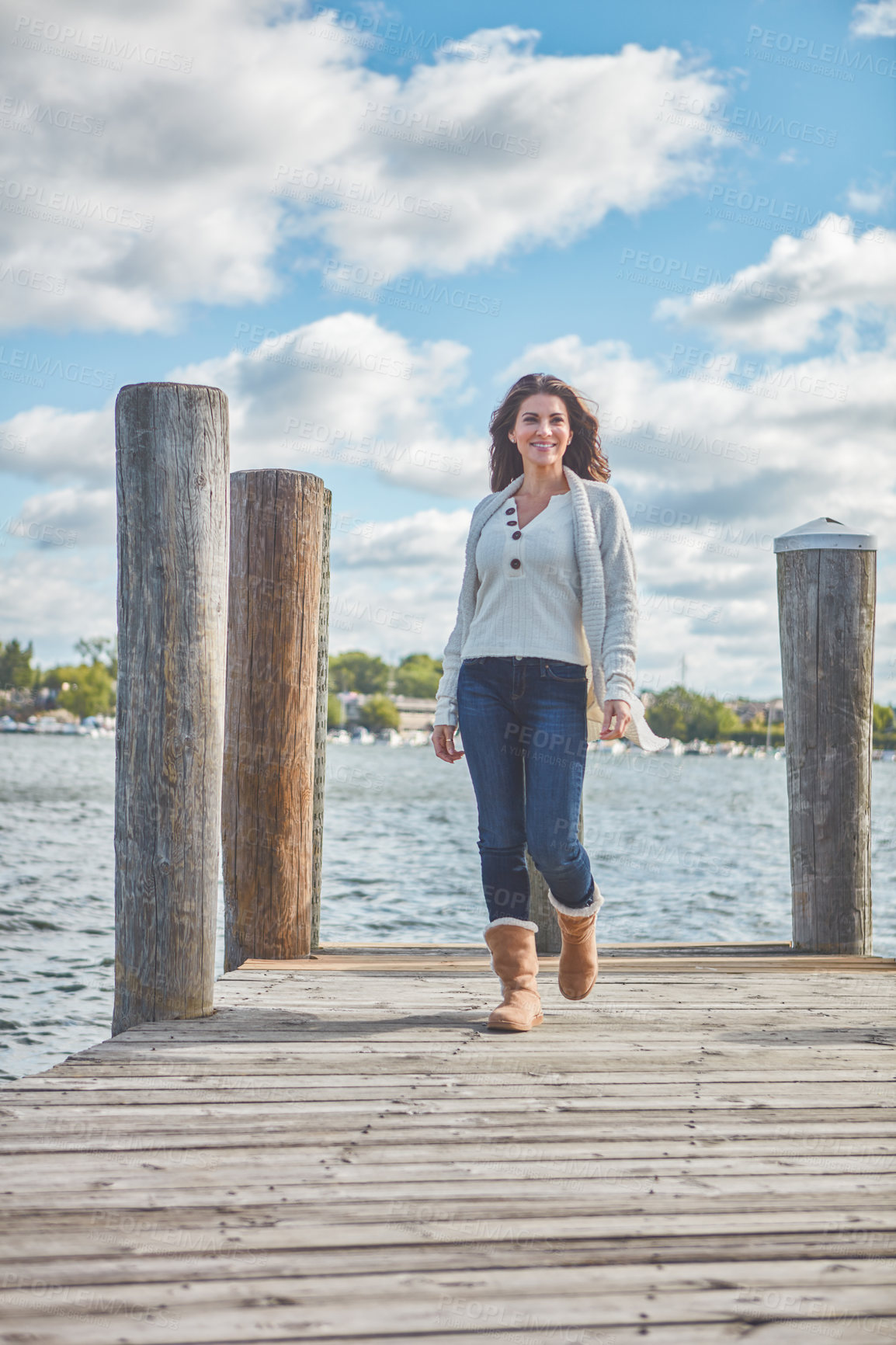 Buy stock photo Shot of a beautiful young woman walking along a pier at a lake