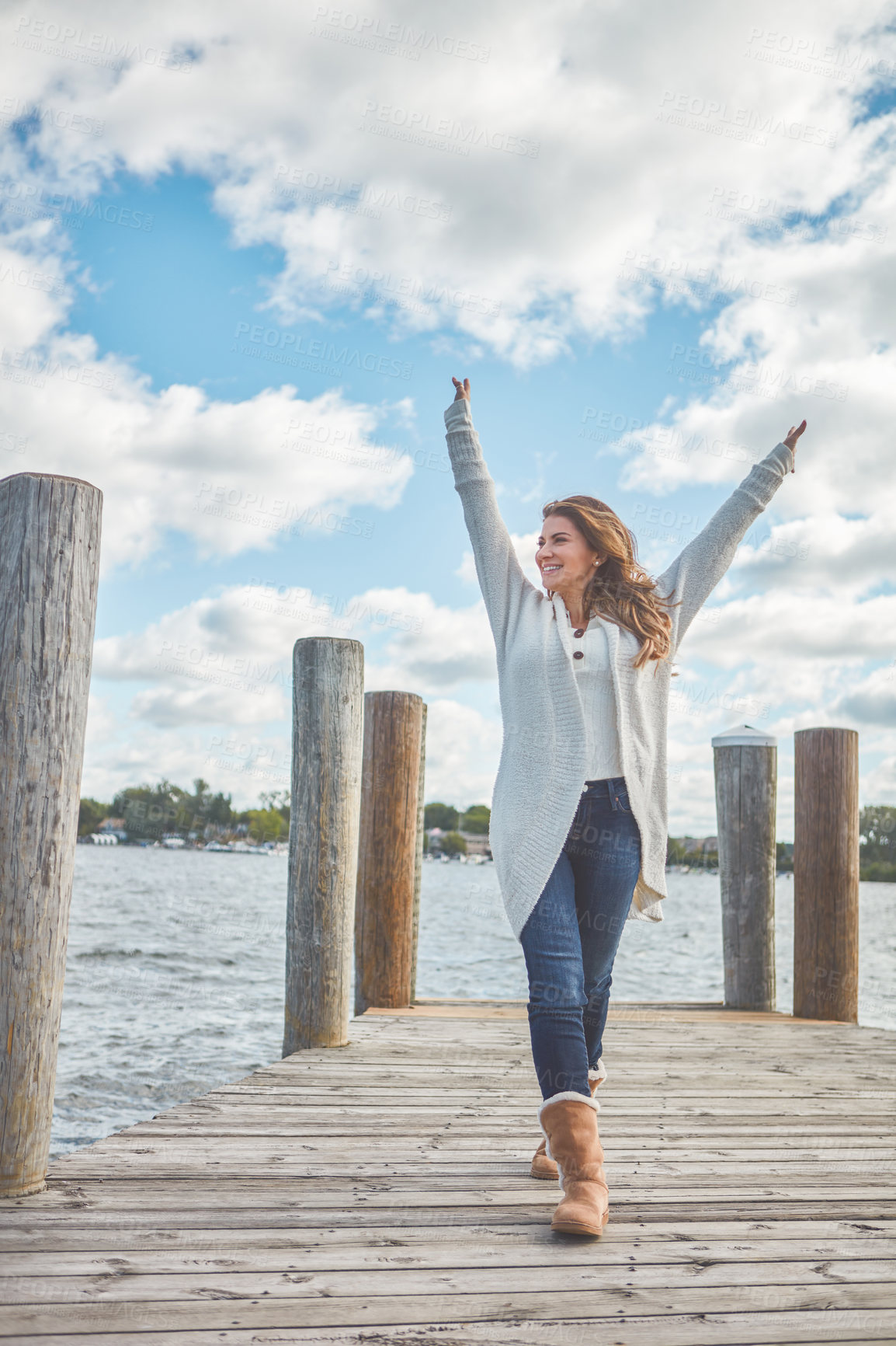 Buy stock photo Shot of a beautiful young woman walking along a pier at a lake