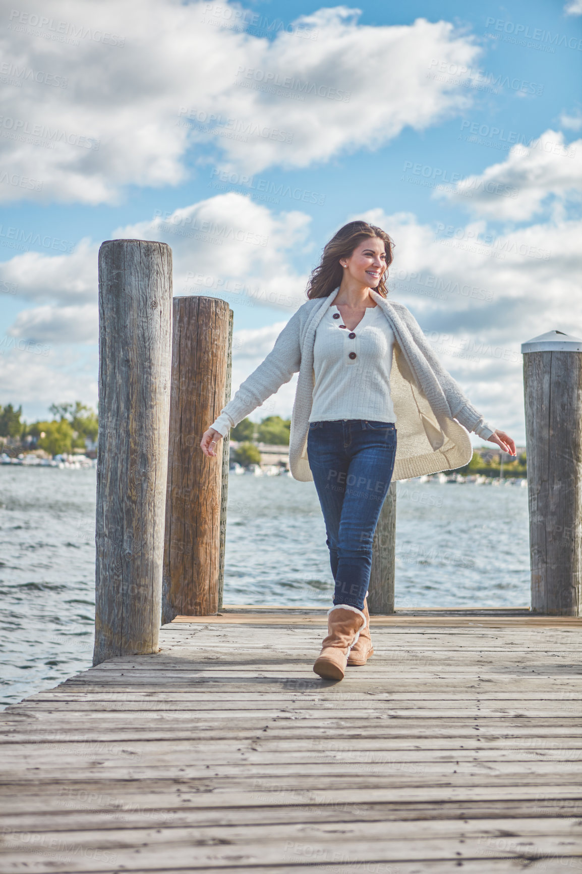 Buy stock photo Shot of a beautiful young woman walking along a pier at a lake