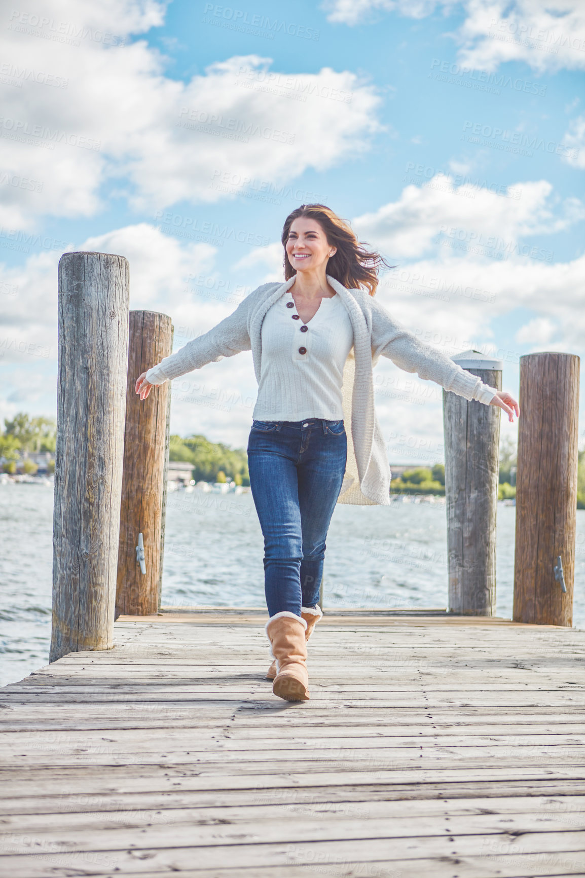 Buy stock photo Shot of a beautiful young woman walking along a pier at a lake