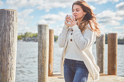 Buy stock photo Shot of a beautiful young woman enjoying a warm beverage on a pier at a lake