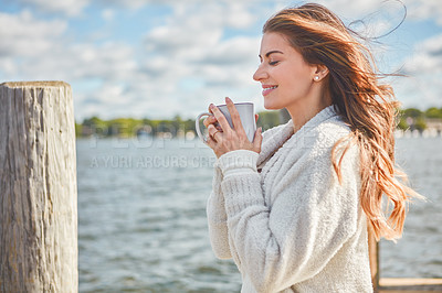 Buy stock photo Shot of a beautiful young woman enjoying a warm beverage on a pier at a lake