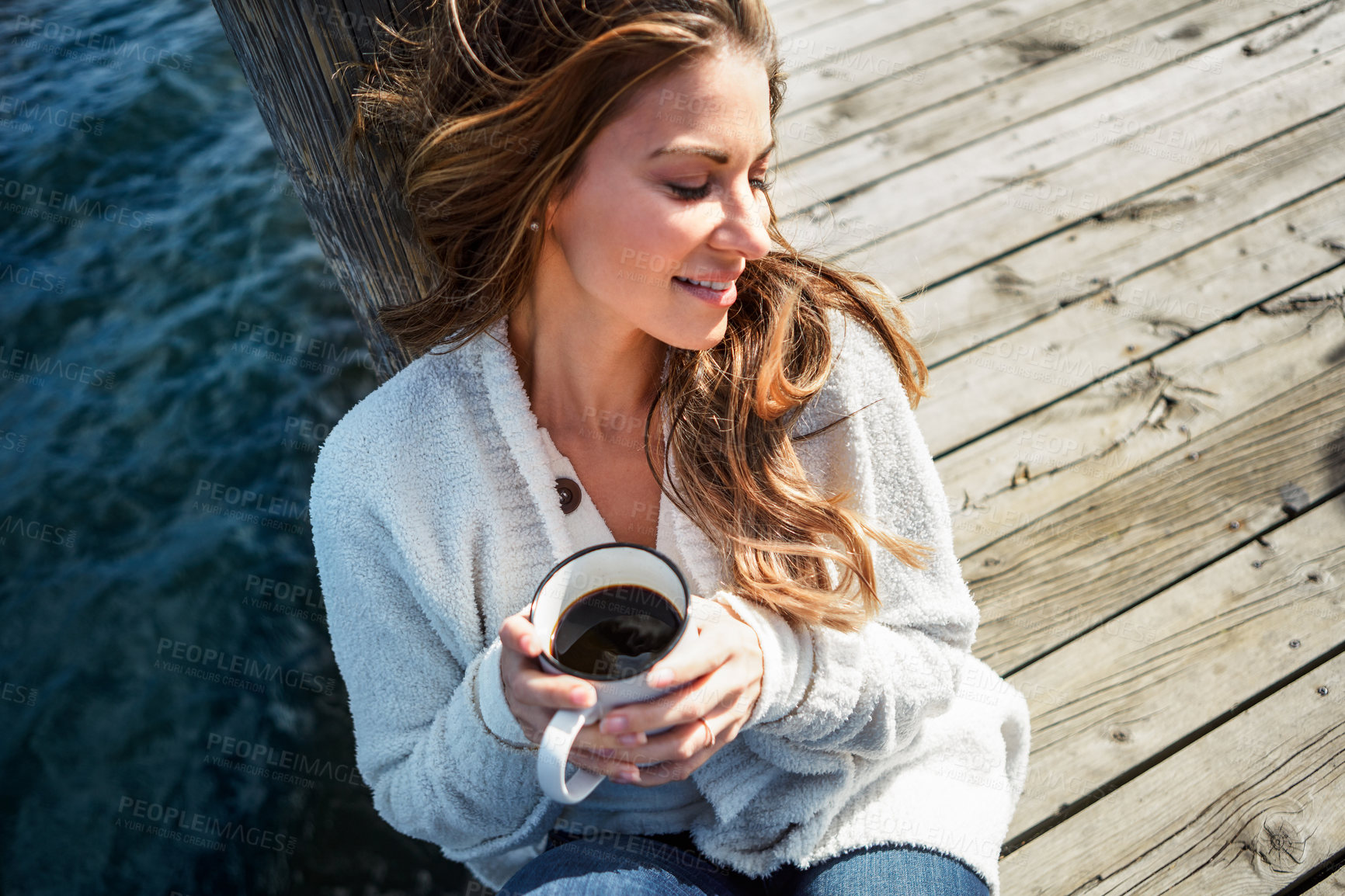 Buy stock photo Shot of a beautiful young woman enjoying a warm beverage on a pier at a lake